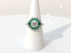 A unique 1 carat transitional round brilliant diamond engagement ring accented by a halo of emeralds.