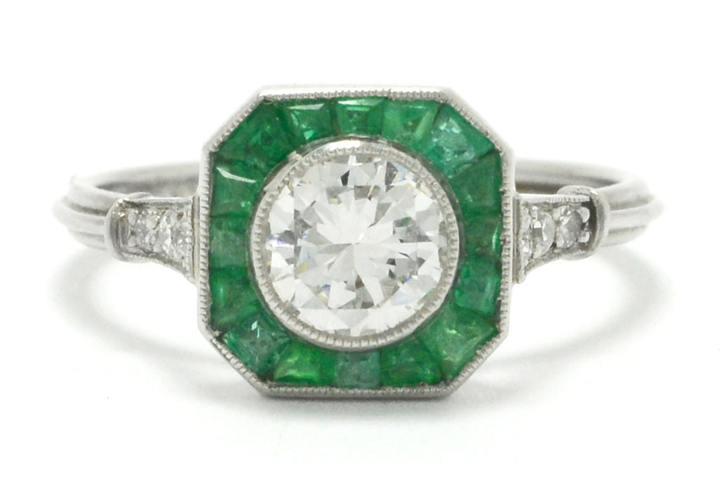 A transitional round brilliant diamond engagement ring with emeralds.