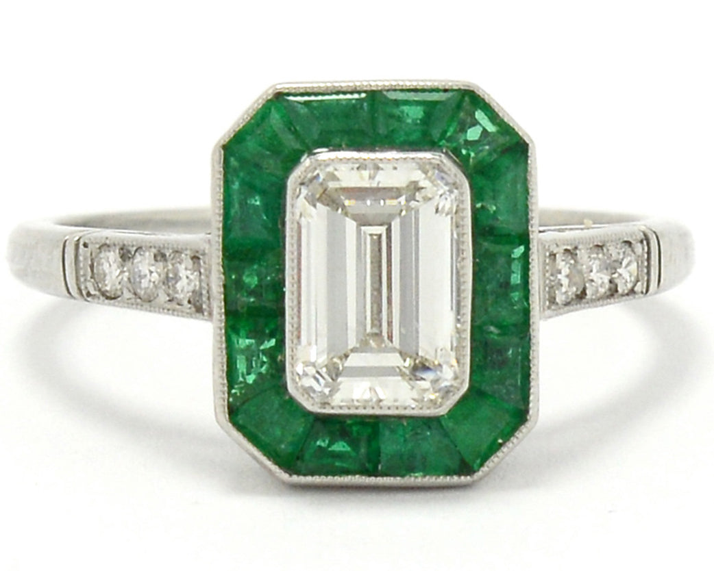 An h color and vs2 clarity 1 carat emerald cut diamond engagement ring with a halo of emeralds.