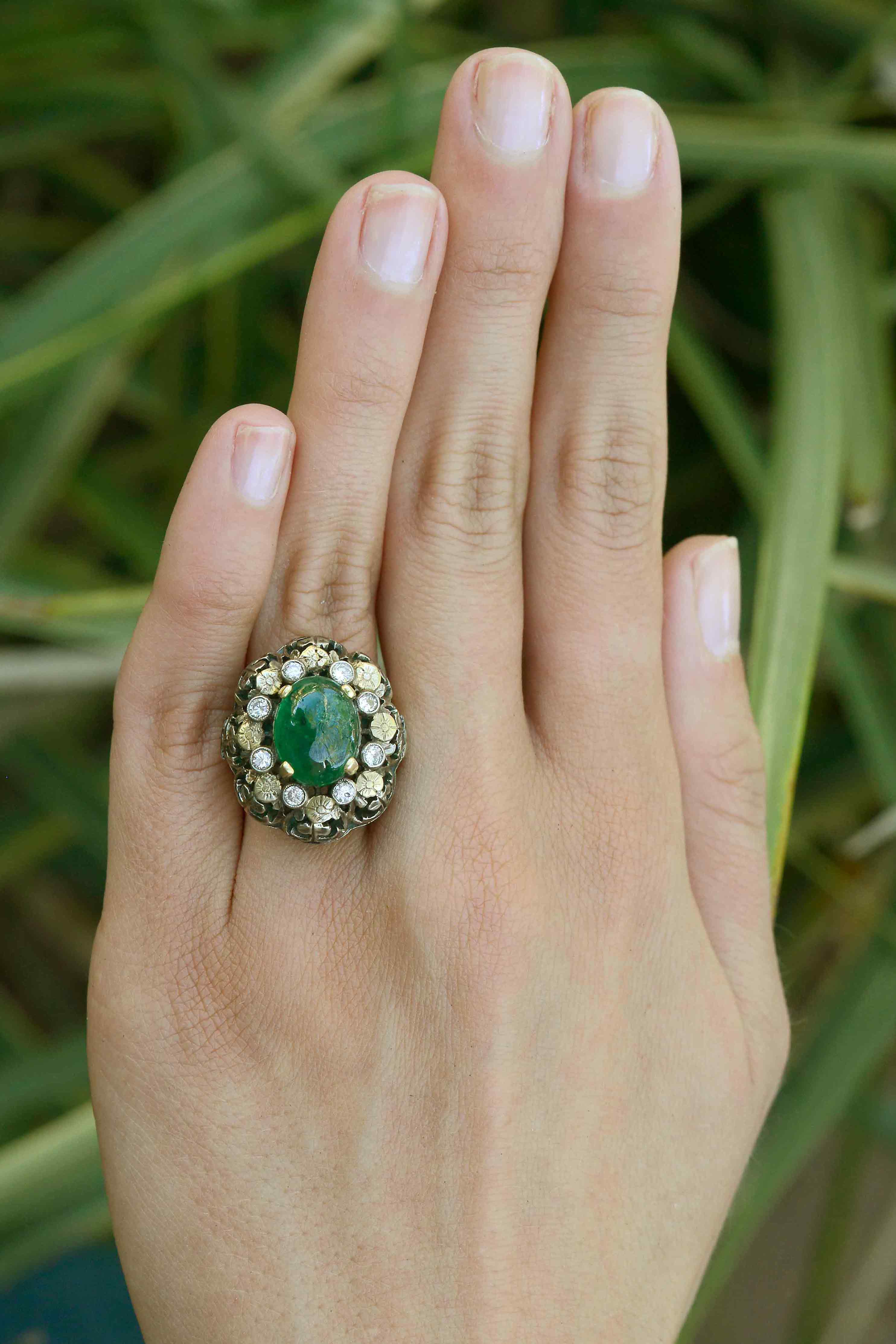 A diamond and flower halo ring with a three carat oval cabochon emerald.