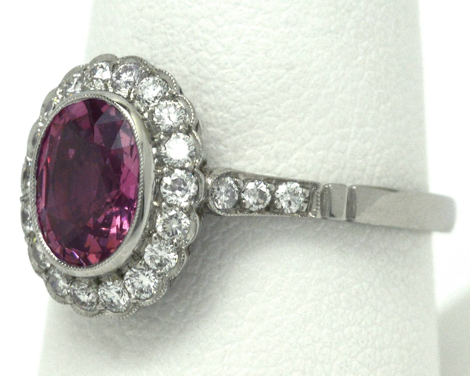 A milgrain diamond halo engagement ring, set with a natural, oval pink sapphire.