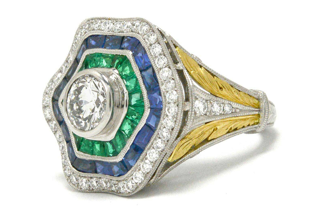A 1 carat round brilliant diamond hexagon ballerina ring with emeralds and sapphires.